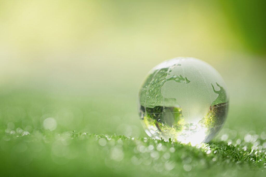 Um globo terrestre feito de vidro está em um solo coberto de grama verde. A luz do Sol atravessa o globo, formando alguns reflexos.