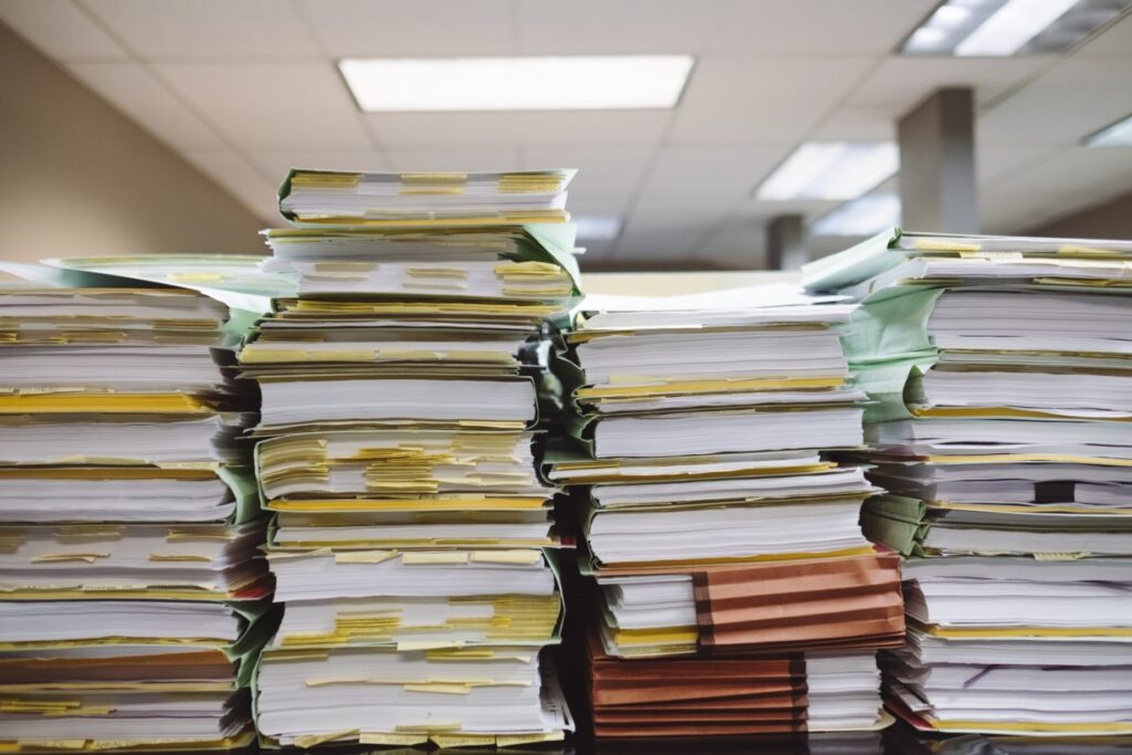 Várias pilhas de documentos sobre uma mesa de escritório.